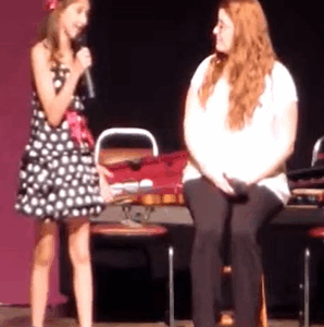 Voice coach Meg O'Brien working with a young student on stage during a singing recital.