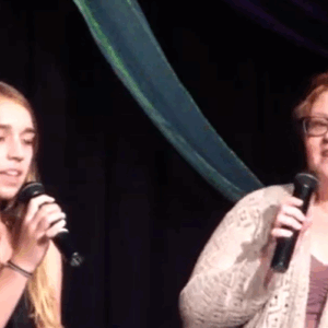 Vocal coach Meg O'Brien singing with a student during a duet performance on stage.